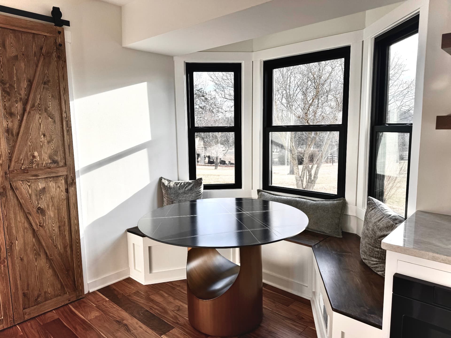 Breakfast nook with built-in bench seating under a bay window and a sliding barn door